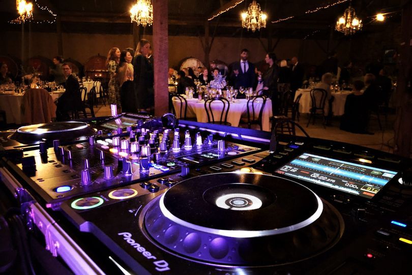 Guests seated for dinner at a barn wedding reception with DJ lighting