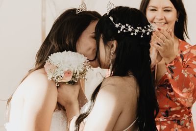 Two brides sharing a kiss as a guest celebrates beside them