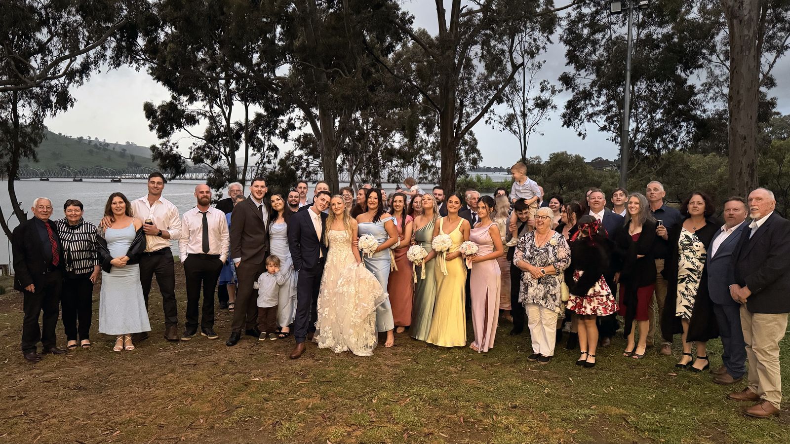 Full wedding party group photo on a lakeside lawn
